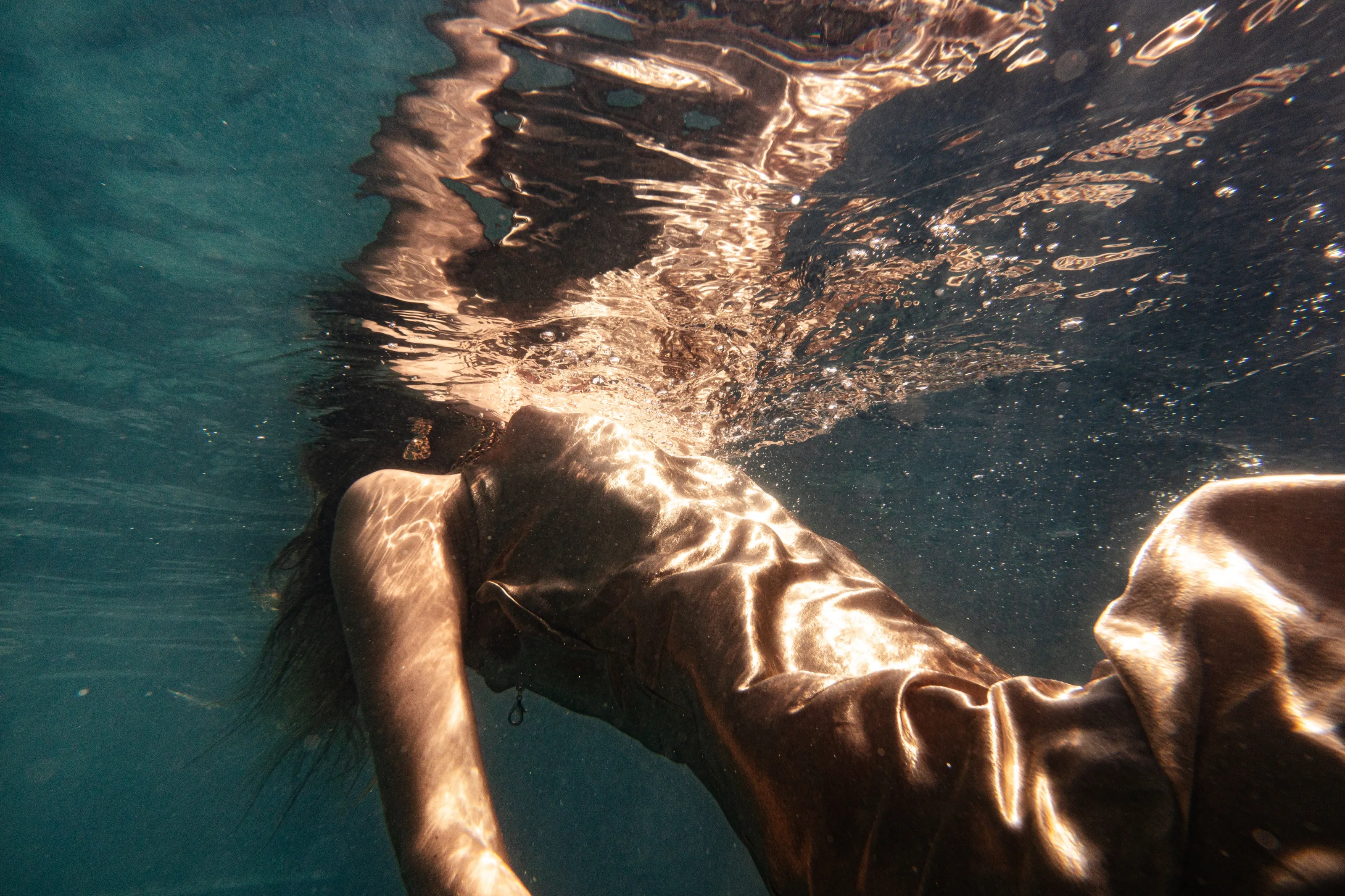 Golden surface light folding across a submerged portrait